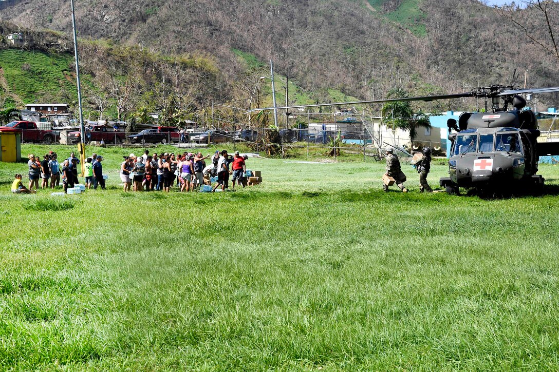A line of people wait nearby a helicopter.