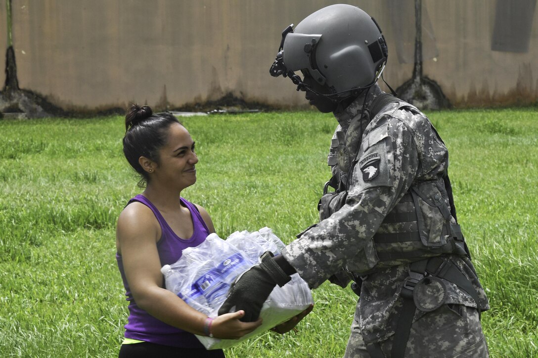 A soldier hands a case of water to a person.
