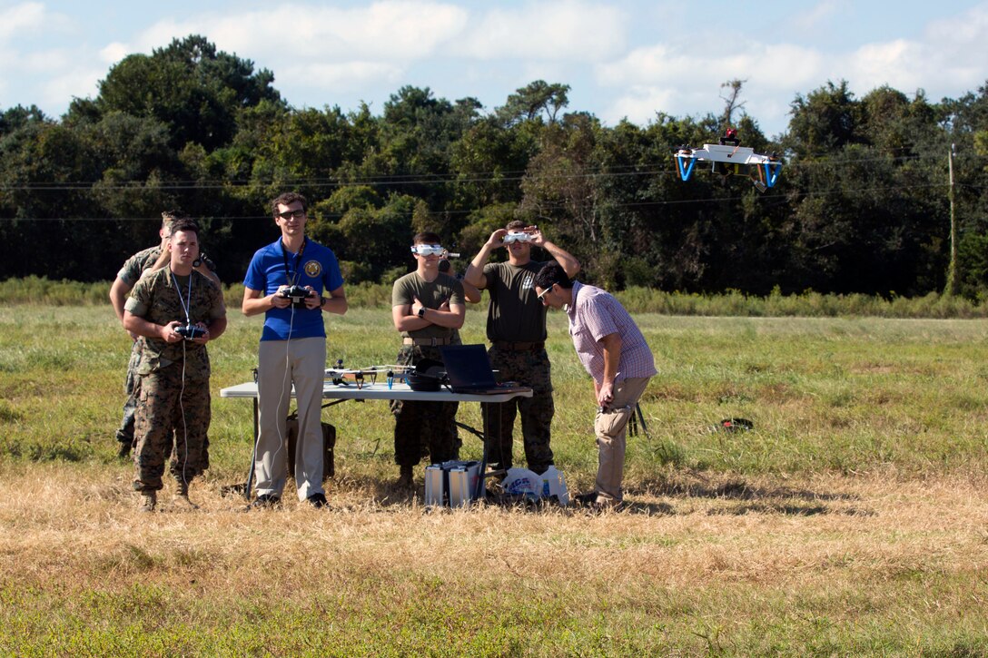 A group of people watch a drone fly in a field.