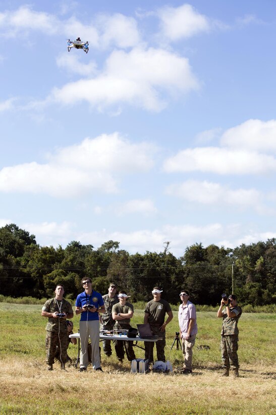 A group of people watch a drone fly in a field.