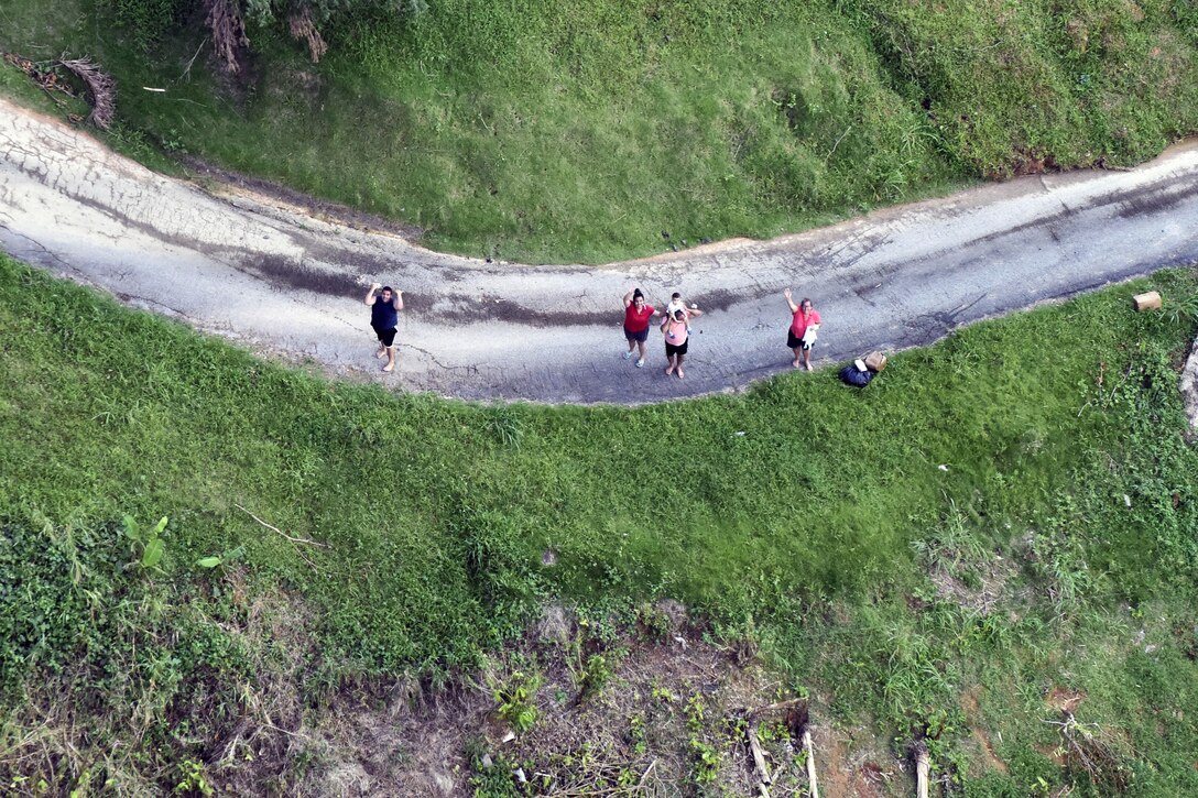 A group of people stand on a dirt road an wave.
