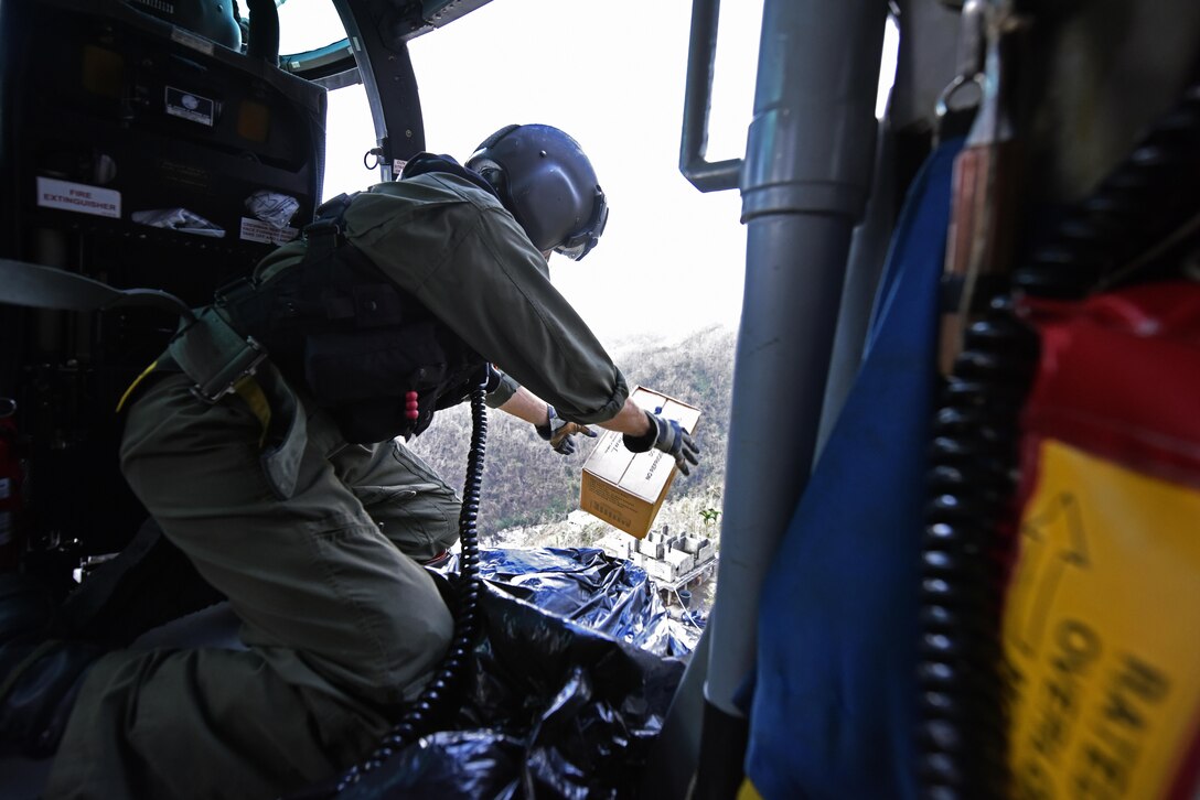 A Coast Guardsman throws a box out an open helicopter door.