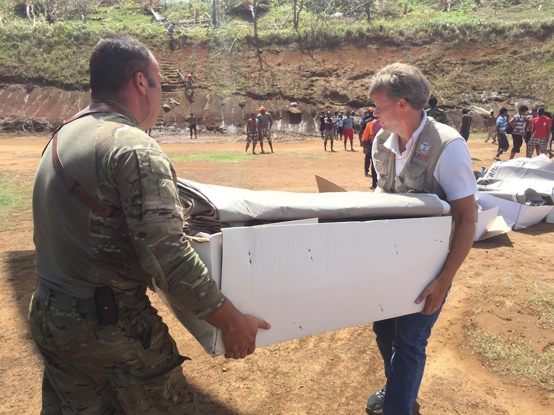 Two people carry a box of supplies from a U.S. Army CH-47 Chinook helicopter at a supply distribution point in Dominica