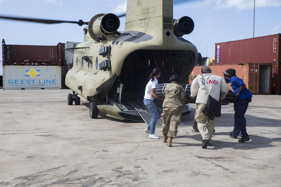 U.S. service members with members of the U.S. Agency for International Development and local citizens load water piping on a U.S. Army CH-47 Chinook helicopter