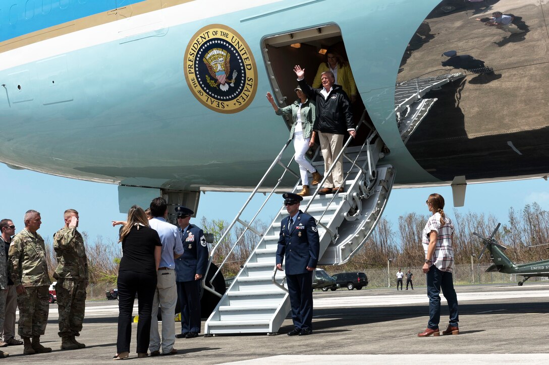 The president and first lady walk down the steps of a airplane.