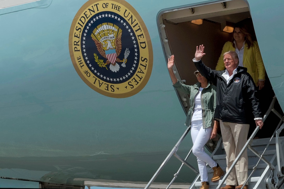 The president and first lady walk out of an airplane with a presidential seal.