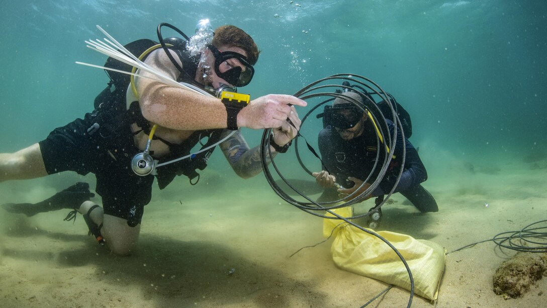 Two divers work with wires underwater.