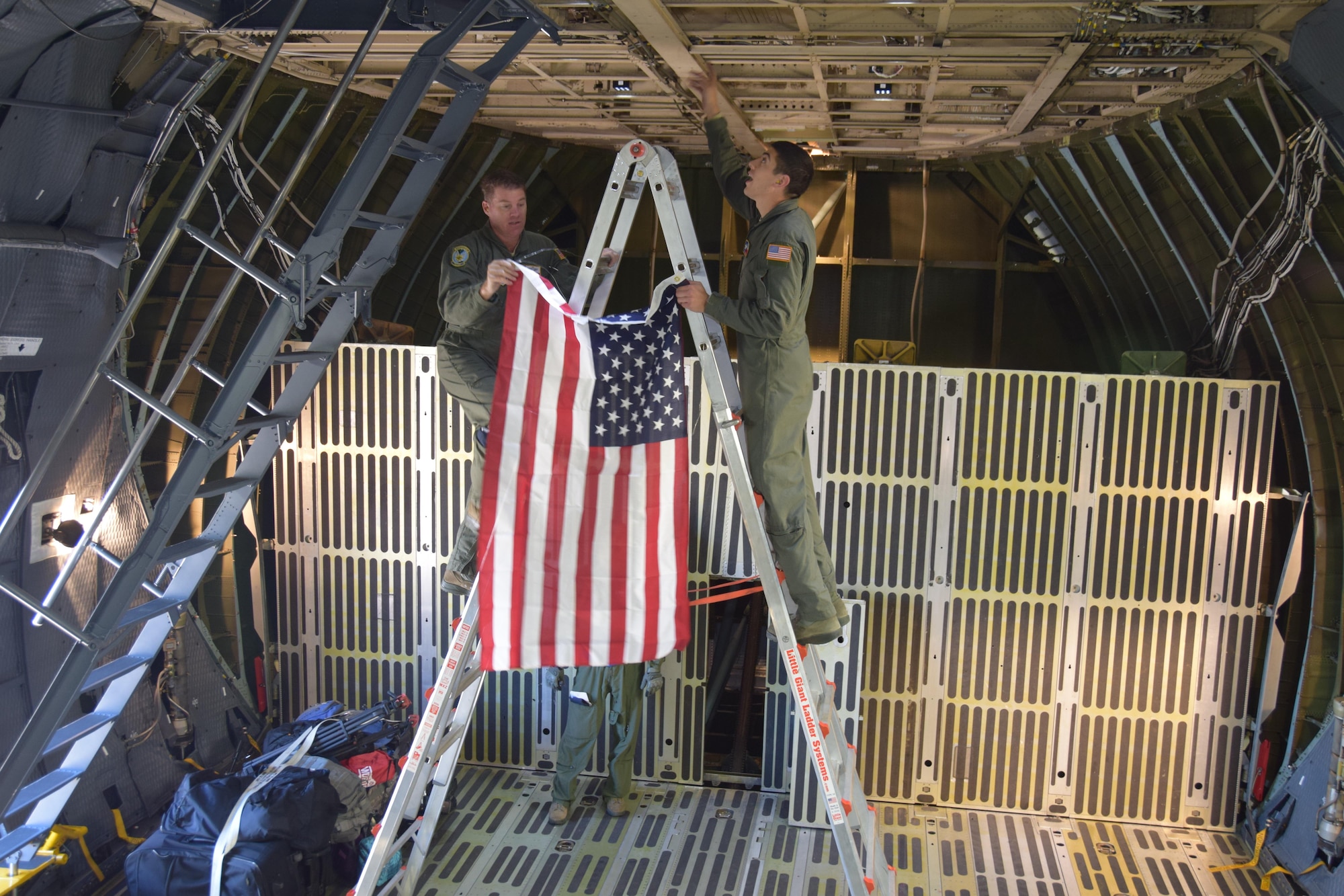 Senior Master Sgt. Kevin Foerster, a 68th Airlift Squadron loadmaster, and Senior Airmen Antonio Farias, a 433rd Aircraft Maintenance Squadron crew chief, climb a ladder to affix a United States flag to the ceiling of an Air Force Reserve Command C-5M Super Galaxy cargo bay prior to takeoff from Colorado Springs, Colorado, Oct. 1, 2017. The 433rd Airlift Wing Citizen Airmen have flown 17 missions to aid hurricane recovery efforts in the United States and its territories to include Puerto Rico and the U.S. Virgin Islands.  (U.S.  Air Force photo by Tech. Sgt. Carlos J. Treviño)