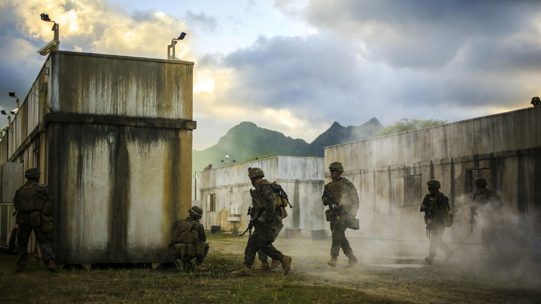Marines move behind a cement structure as smoke billows around them.