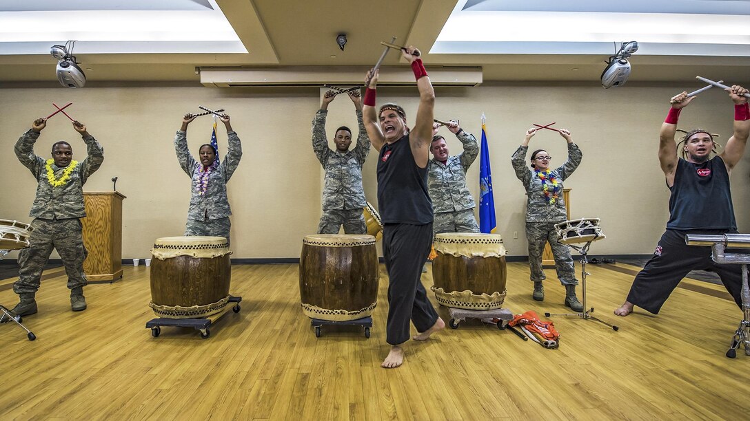 Airman standing in front of drums hold up drumsticks.