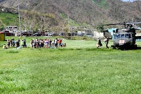 A line of people wait nearby a helicopter.