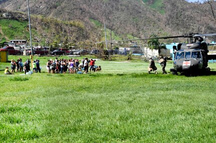 A line of people wait nearby a helicopter.