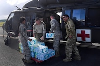 Four soldiers pick up cases of water and put them into helicopters.