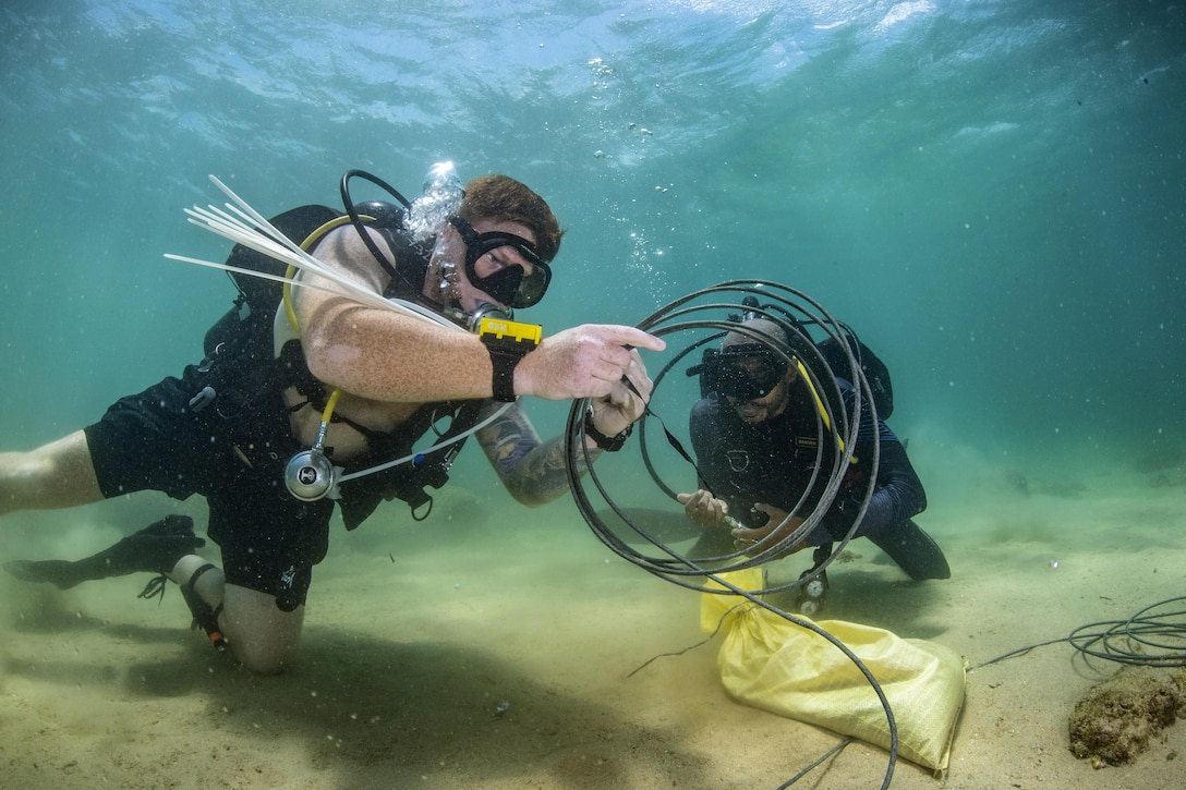 Two divers work with wires underwater.