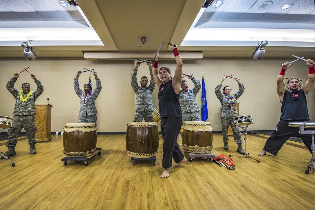 Airman standing in front of drums hold up drumsticks.