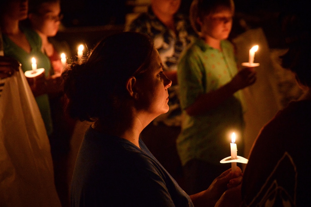 A person holding a candle is surrounded by others holding candles.