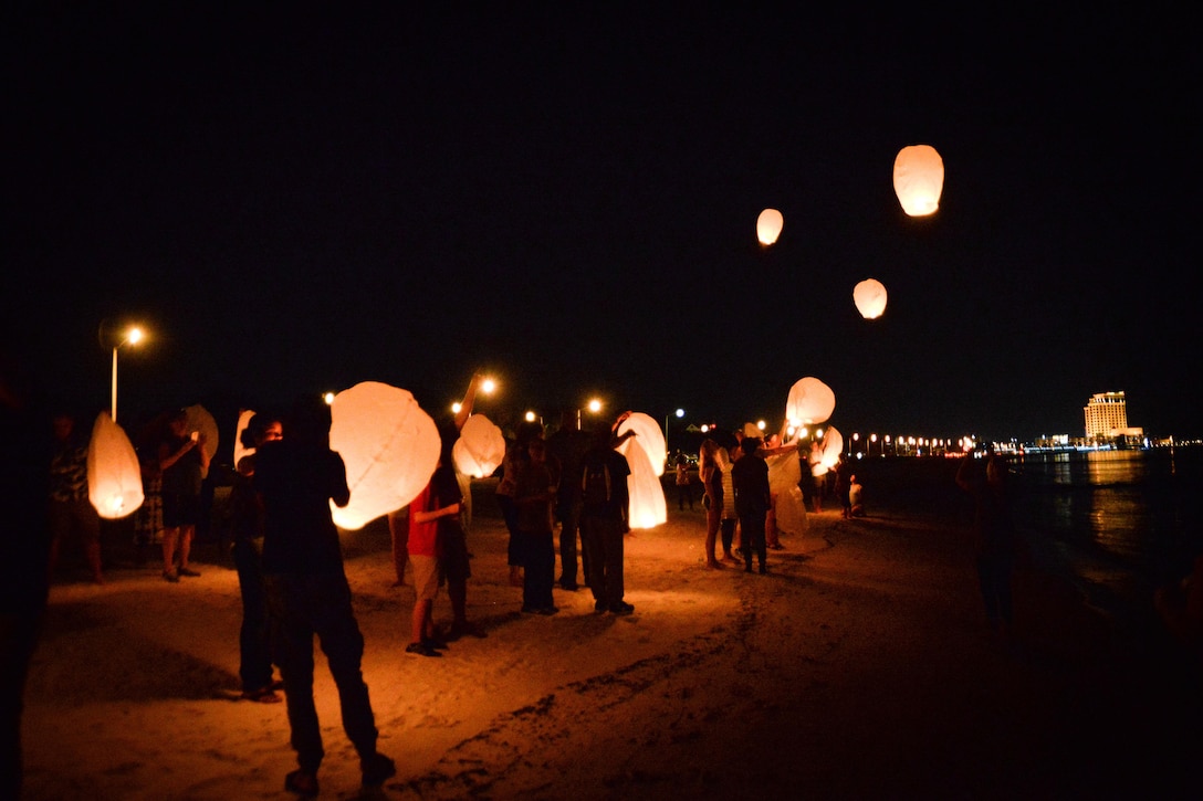 A group of people release flying lanterns into the night sky.
