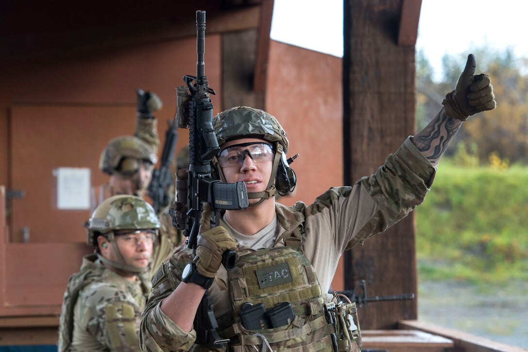 An airman holding a firearm gives a thumbs up signal.