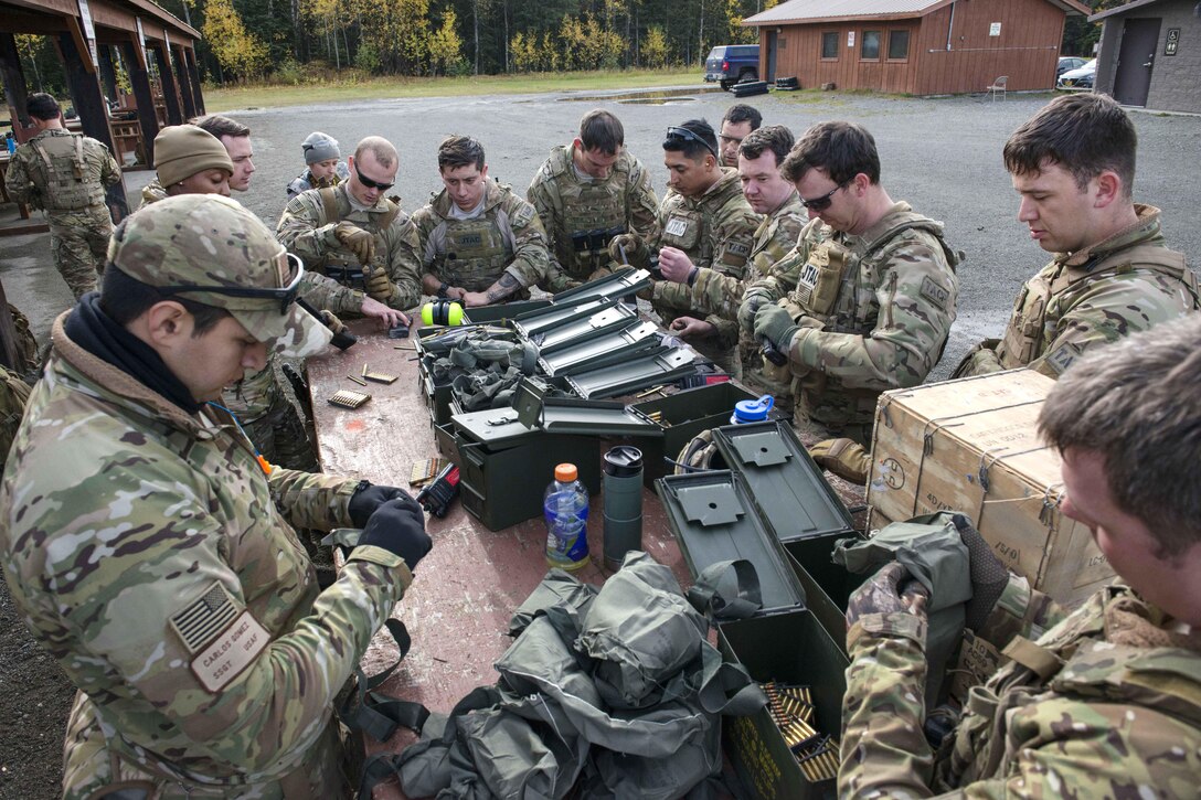 A group of airmen around a table with amo boxes load firearms.