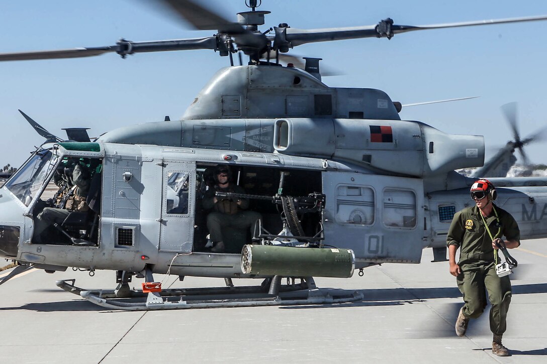 A Marine sits in a helicopter while another walks away from it.