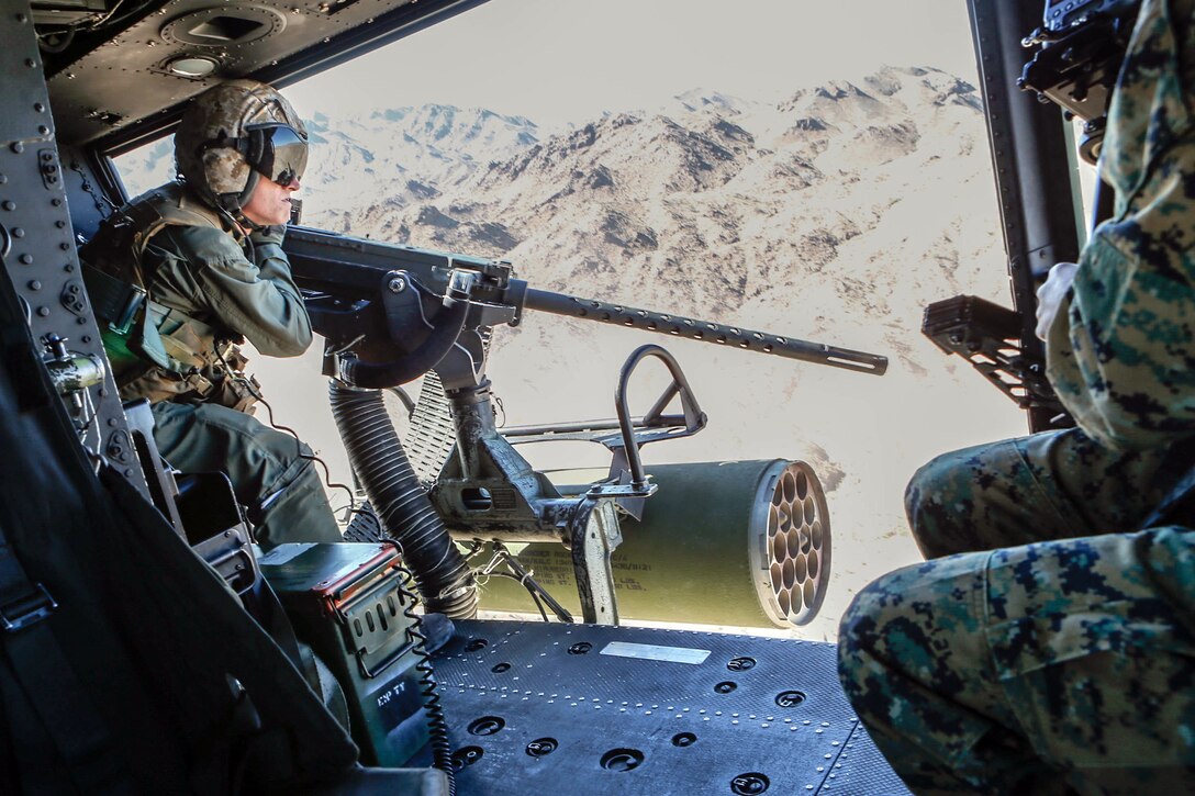 A Marine aims a weapon out an open helicopter door.