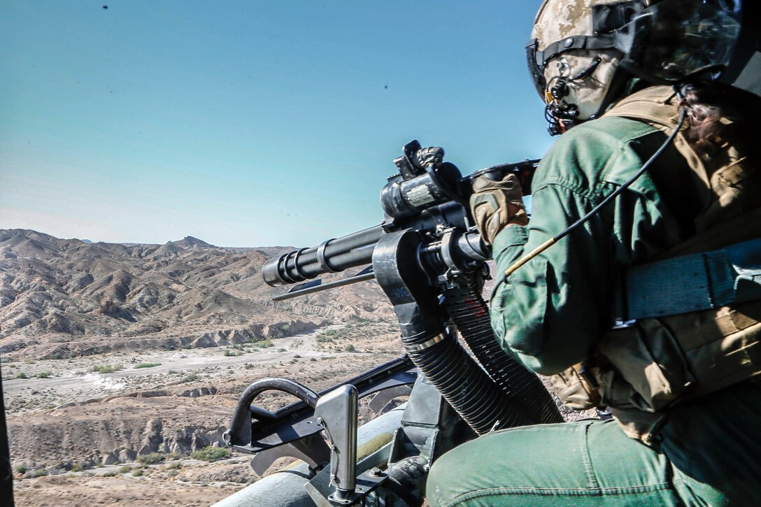 A Marine aims a firearm in the desert.
