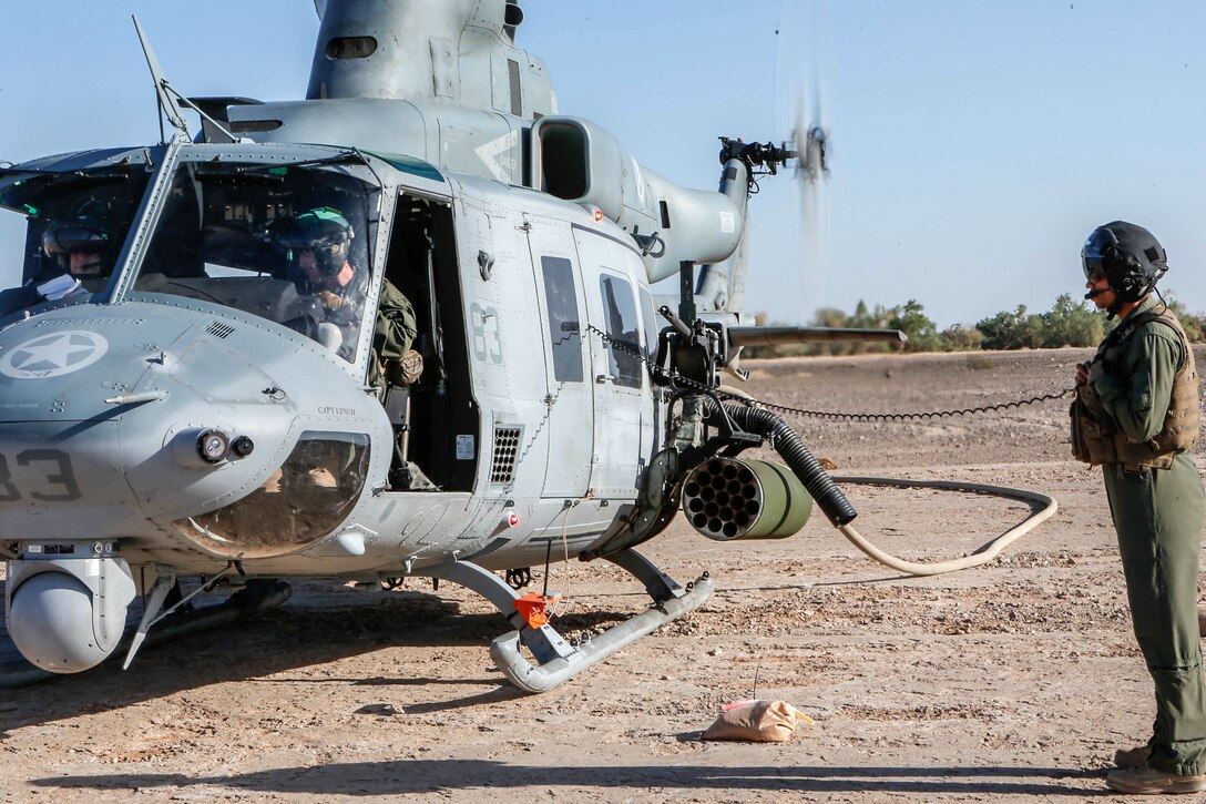 A helicopter sits on the ground with a hose running to it.