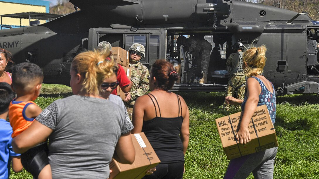 Soldiers deliver boxes of aid to residents following a hurricane.