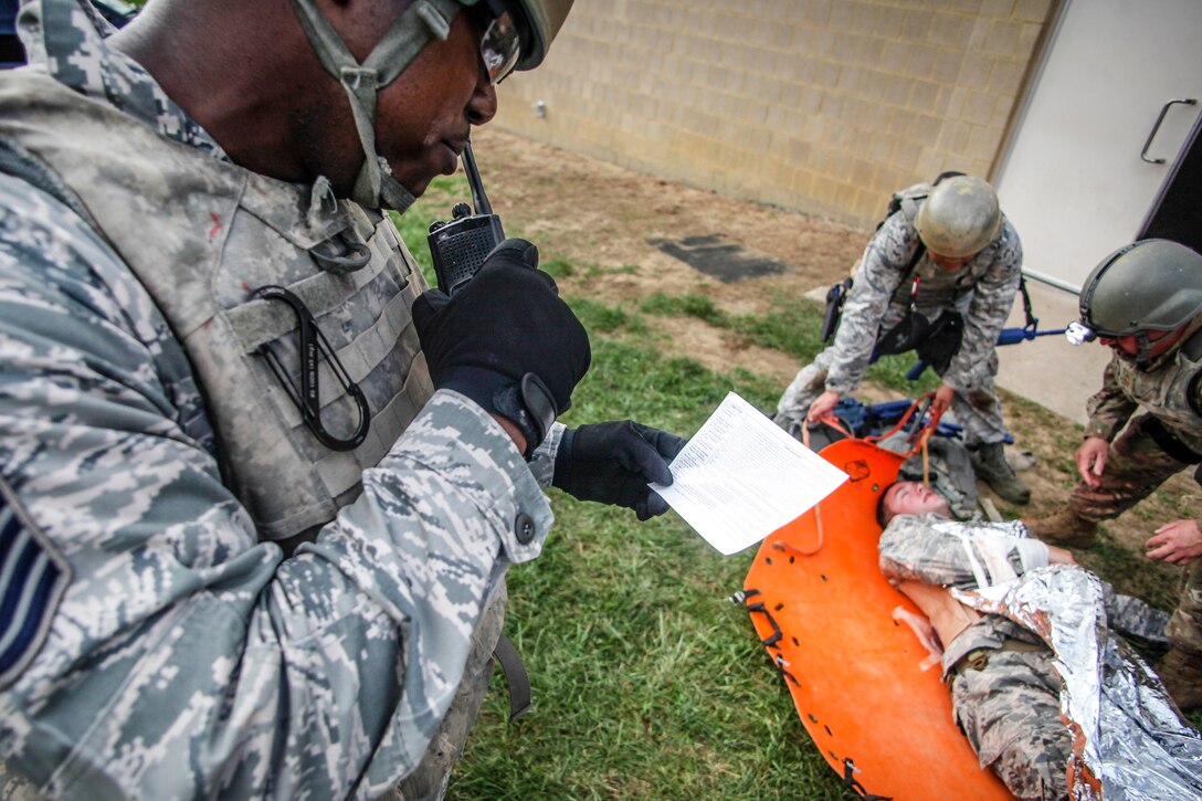 An airman calls in a medical report while airmen prepare to evacuate a simulated patient.