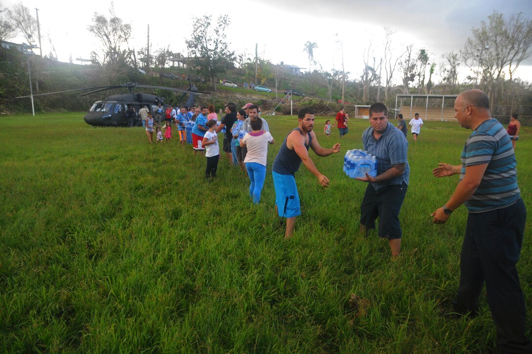 A line of civilians help unload cases of water from a helicopter.
