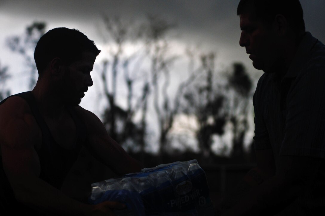 A guardsman hands a case of water to a person.
