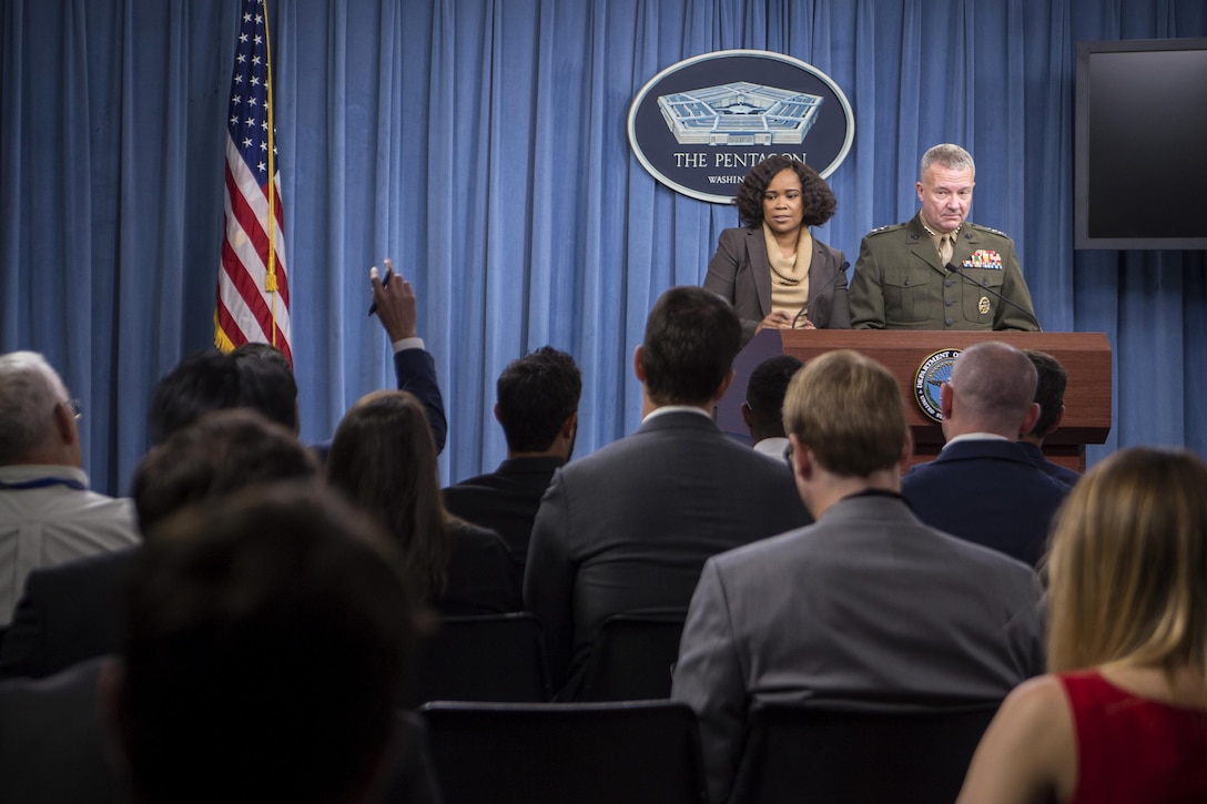 A civilian and a Marine general stand behind a podium.