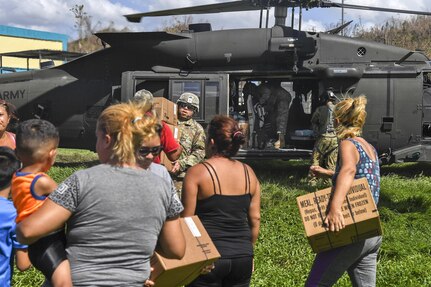 Soldiers deliver boxes of aid to residents following a hurricane.