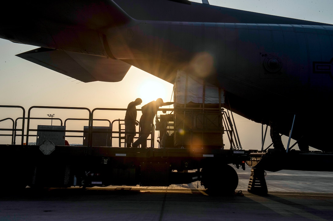 Two airmen push cargo.