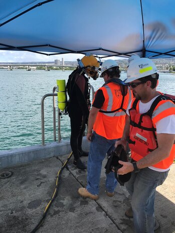 Diver Max Schramm undergoes pre-inspection safety checks before a dive with the help of Erick Knezek, dive tender and owner of Truston Technologies, and Trent Webster, dive supervisor. The dive was part of an operation that took place Aug. 28 through Sept. 1 to repair the marine oil booms at the Pearl Harbor Hotel Pier off the Hawaiian island of Oahu.