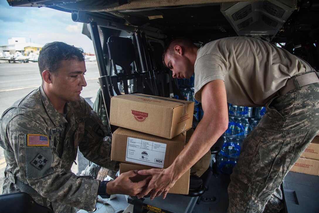 Army Sgt. 1st Class Alexander Blake, left, and Spc. Cody Nelson, both assigned to the 101st Combat Aviation Brigade of the 101st Airborne Division, load an UH-60 Black Hawk with food and water.