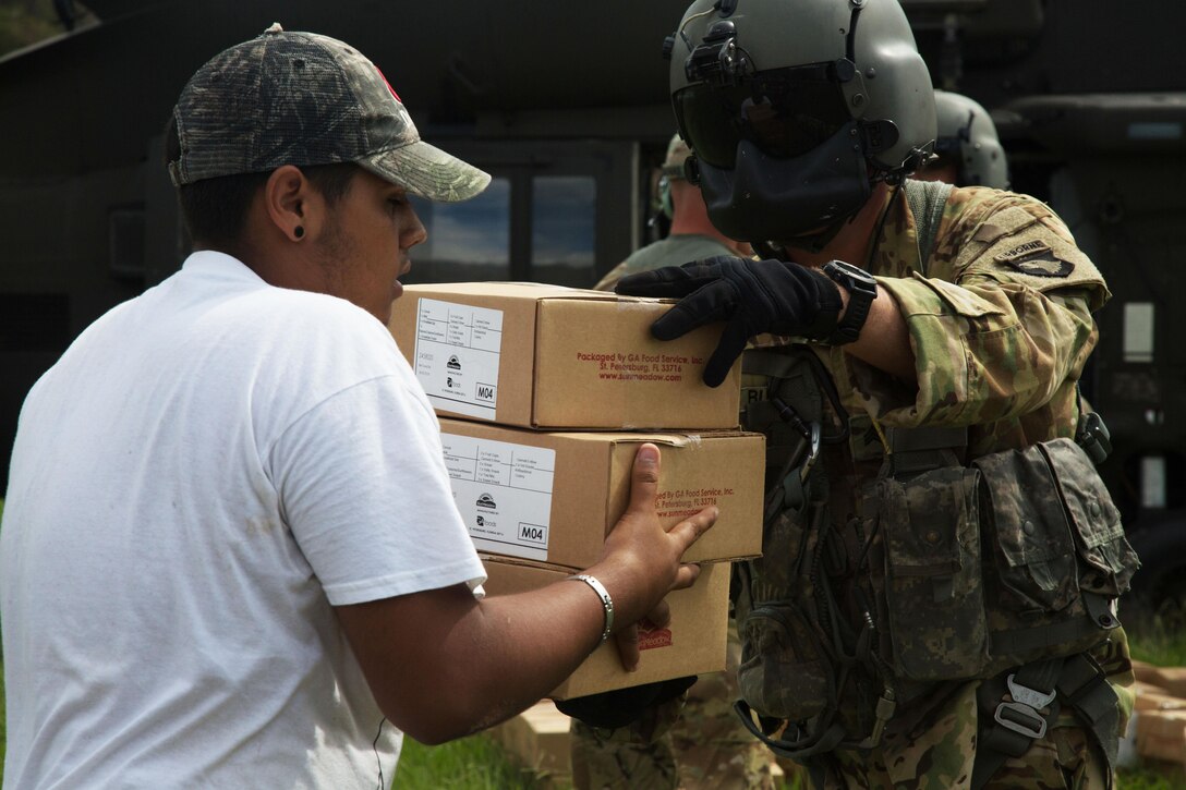 A soldier hands boxes of food and supplies to a resident.