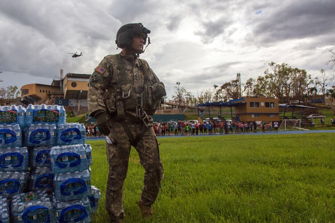 Army  Sgt. 1st Class Alexander Blake, assigned to the 101st Combat Aviation Brigade, 101st Airborne Division, stands near cases of water to be distributed.