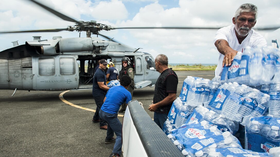 Sailors and others unload relief supplies from a helicopter.