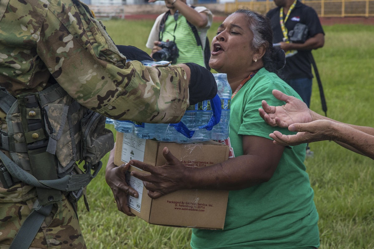 A soldier hands water and food to a woman.