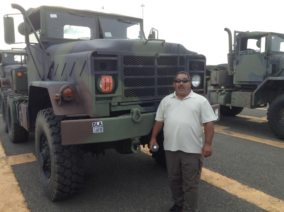 A man stands in a parking lot next to a truck nearly twice as tall as he is