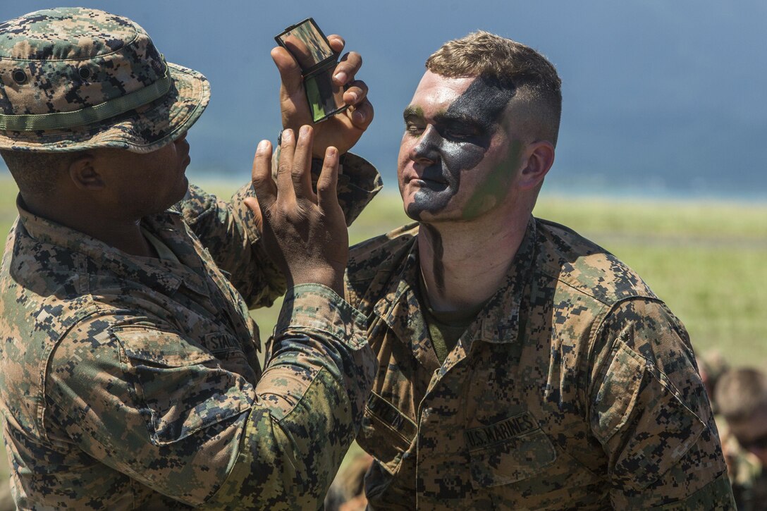 A Marines puts face paint on another Marine.