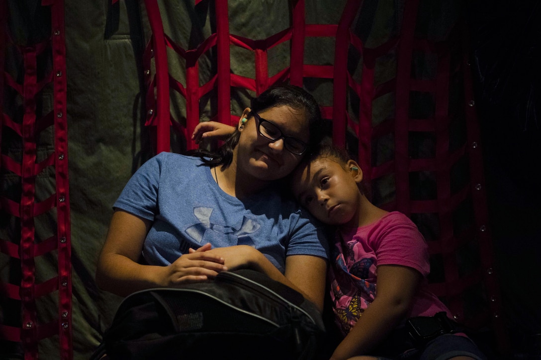 A woman and girl lean against each other while resting in a plane.