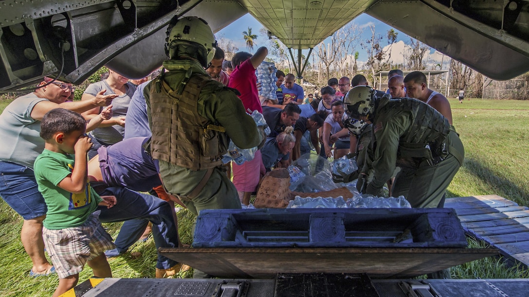 A group of people pick up water and other supplies behind an aircraft.