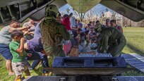A group of people pick up water and other supplies behind an aircraft.