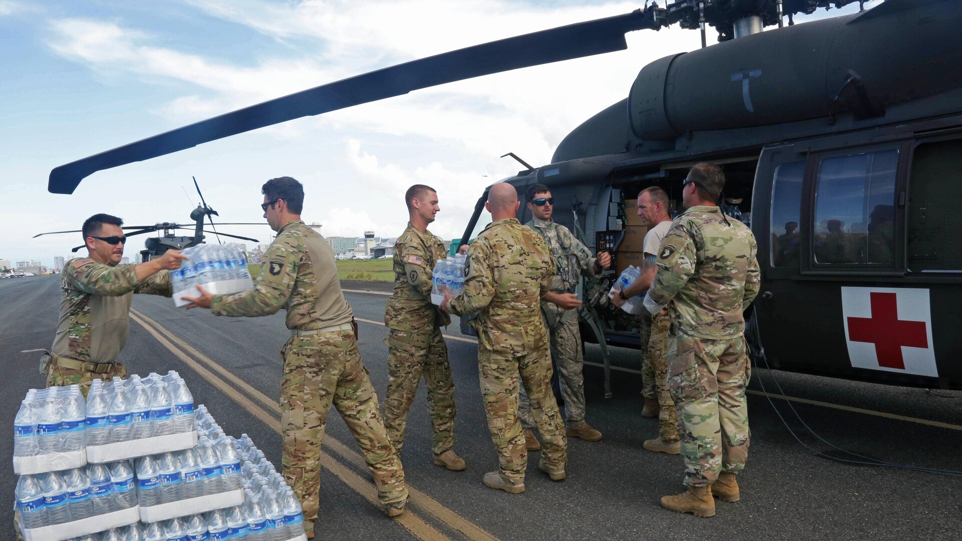 A group of service members hand off water cases to each other next to a helicopter.