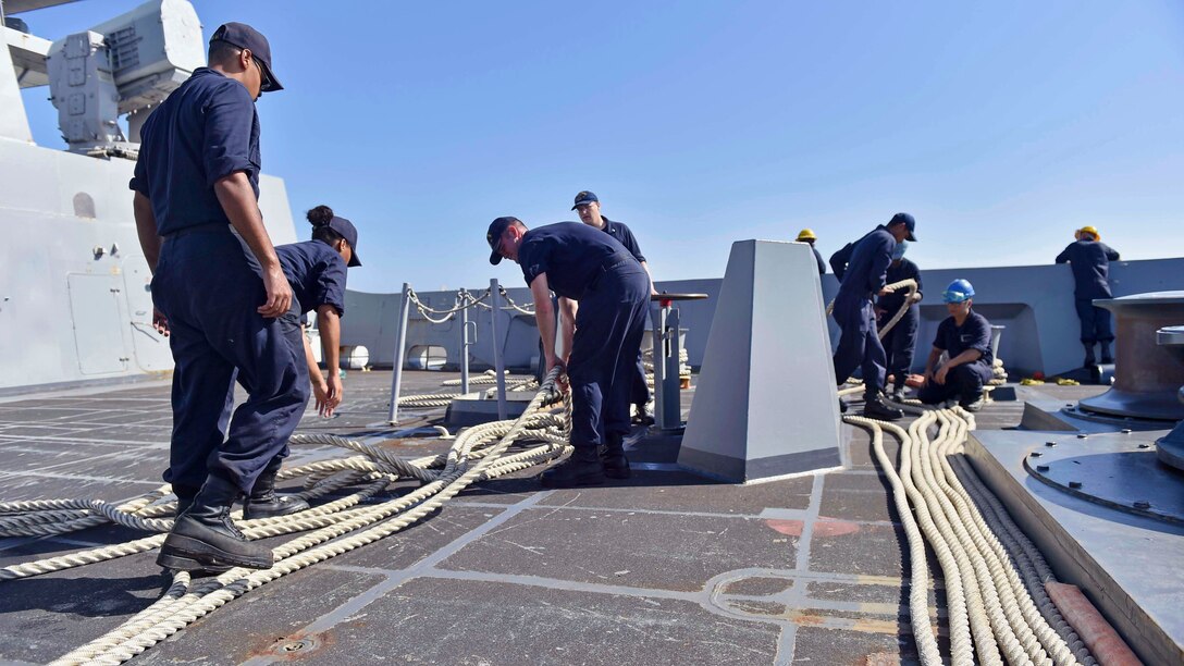 A group of Sailors inspect mooring lines on the deck of a ship.