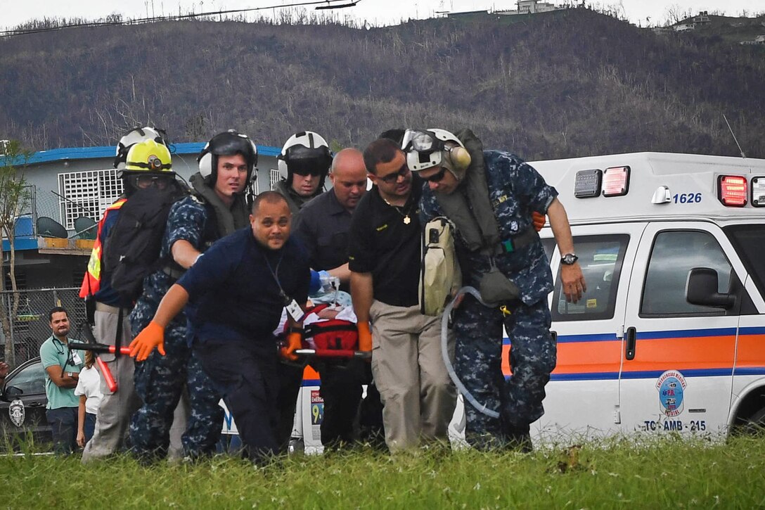 Sailors and other medical personnel move a patient on a stretcher.