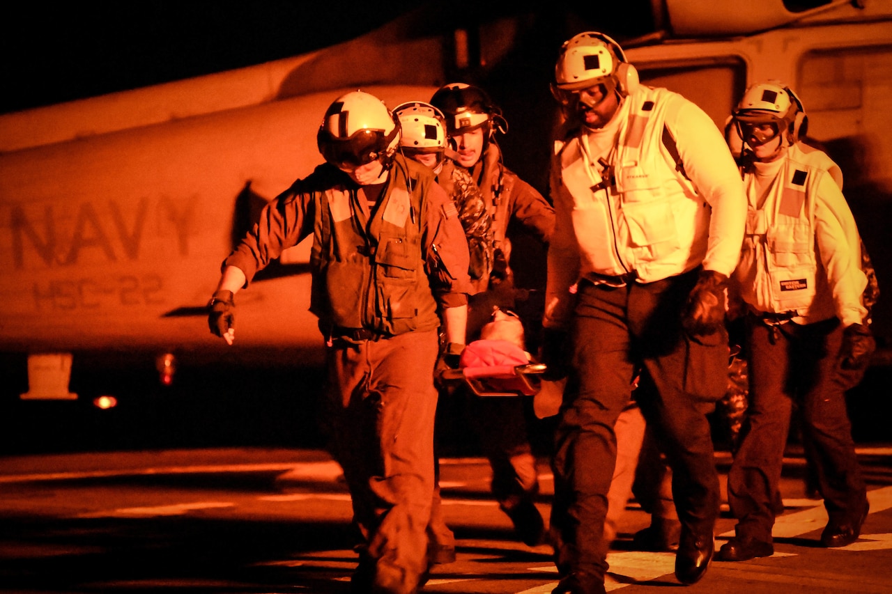 Sailors carry patient from helicopter on a stretcher.