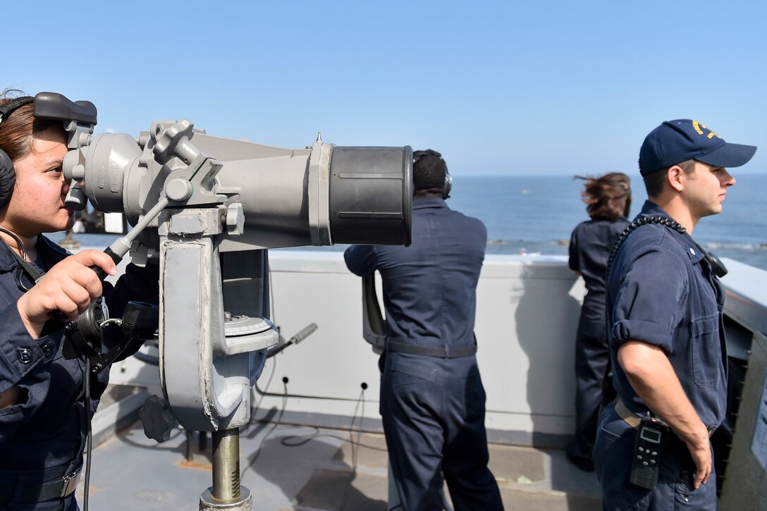 A sailor looks through binoculars.